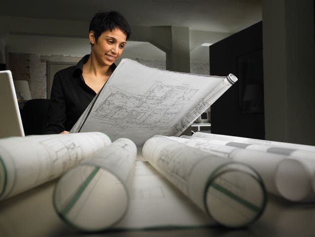 Female architect reading blueprint at desk