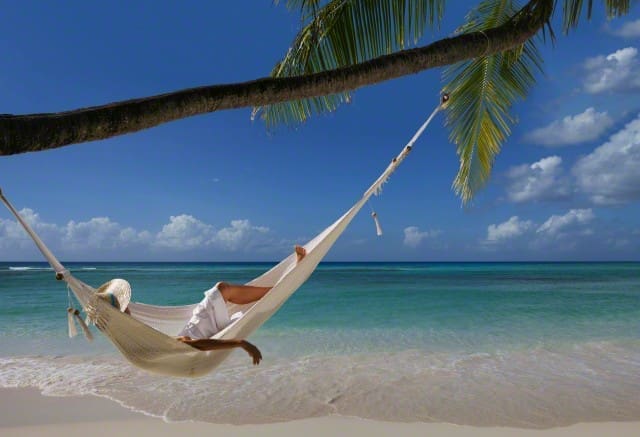 Caucasian woman laying in hammock under palm tree on tropical beach